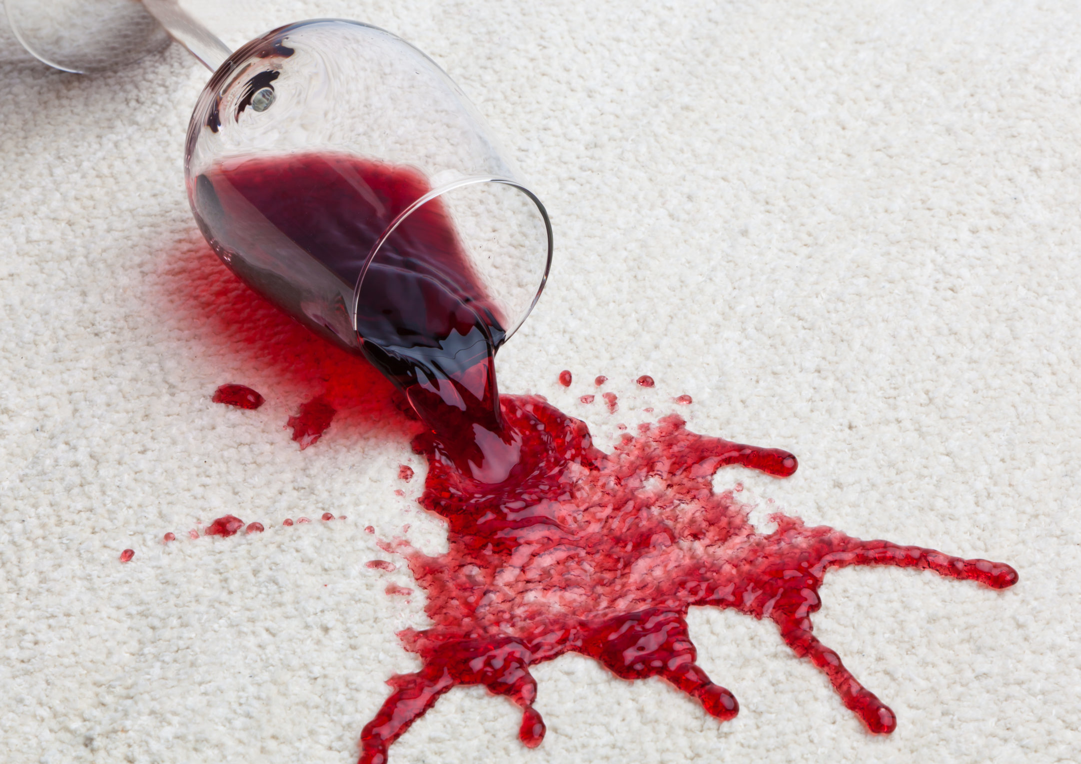 A glass of red wine spilling onto a clean white carpet